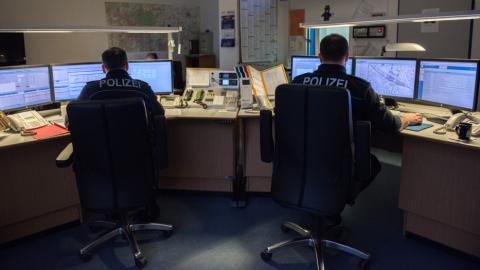 Zwei Polizisten sitzen am Schreibtisch. Jeder arbeitet an drei Monitoren